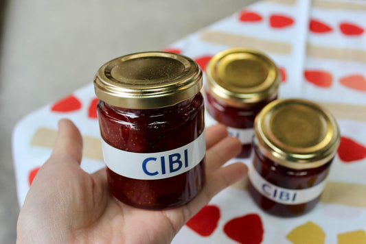 Assorted strawberry jam and granola gift set in a fabric pouch, featuring jars of jam and a bowl of granola, on a wooden surface.